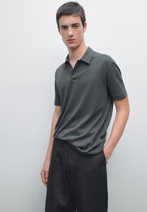 Mörkgrön polo skjorta med klassisk krage, korta ärmar och tvåknapps placket, i kombination med svarta byxor. Slät tygstruktur.