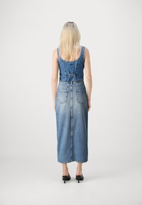 Farmernadrág ruha, fókuszált felsőrésszel, állítható pántokkal és hosszú szoknyával. Nos, világoskék, kopott hatású, hátul zsebekkel. 
