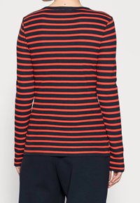 Maglietta a maniche lunghe realizzata in morbido tessuto con righe orizzontali blu navy e rosse. Presenta un collo rotondo e una silhouette aderente.