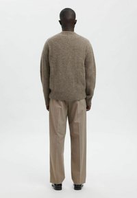 Brun genser i ullblanding med rund hals, ribbestrikket kant og lange ermer; kombinert med lyse beige skreddersydde bukser og svarte sko.