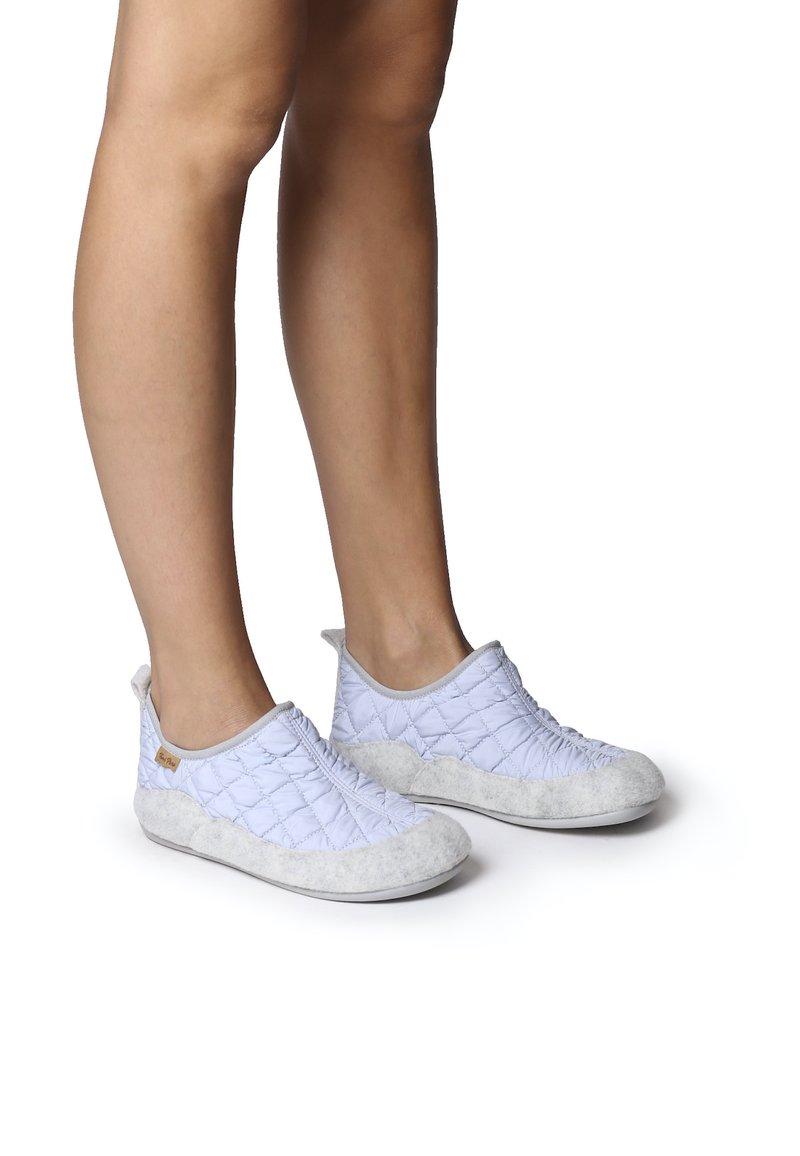 Quiltade ljusblåa slip-on skor med en mjuk grå mockadetalj vid tån och hälen, med elastiska sidopaneler för enkel påtagning.