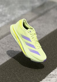 Scarpa da corsa leggera in giallo neon con accenti viola, tomaia in rete texturizzata e suola ammortizzata. Presenta il design con tre strisce.