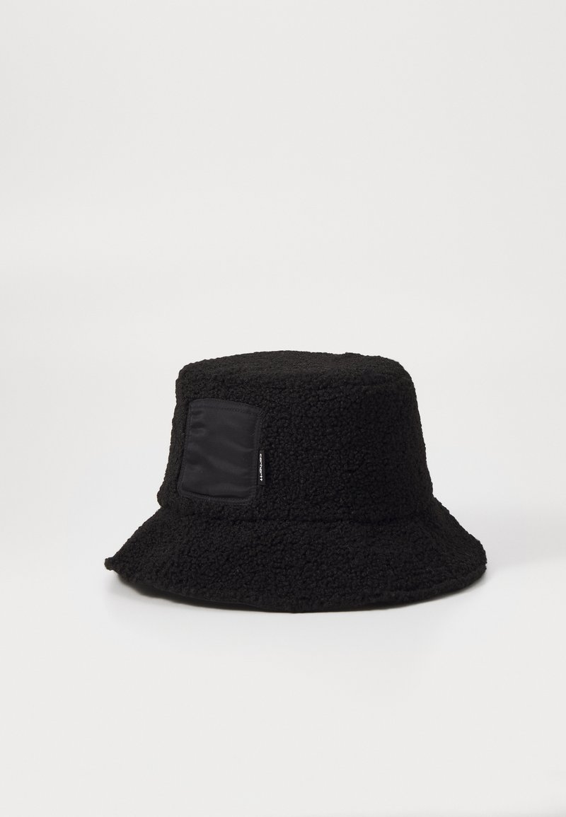 Sort bucket hat lavet af tekstureret stof med en blød, fuzzy følelse; har en flad top og et rektangulært sort patch på siden.