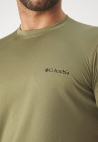 Camiseta de manga corta color verde oliva, fabricada en tejido suave, con un logo negro de Columbia en la parte izquierda del pecho.