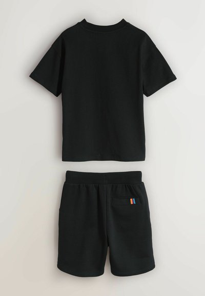 T-shirt noir à manches courtes associé à un short noir à taille élastique avec une petite poche dotée d'une étiquette rayée colorée à l'arrière.