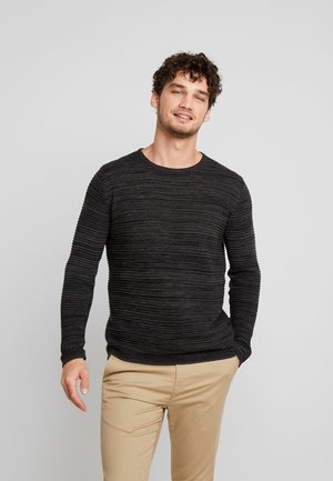 Dunkelgrauer gestrickter Pullover mit vertikaler Rippstruktur, Rundhalsausschnitt und langen Ärmeln. Kombiniert mit hellbraunen Hosen.