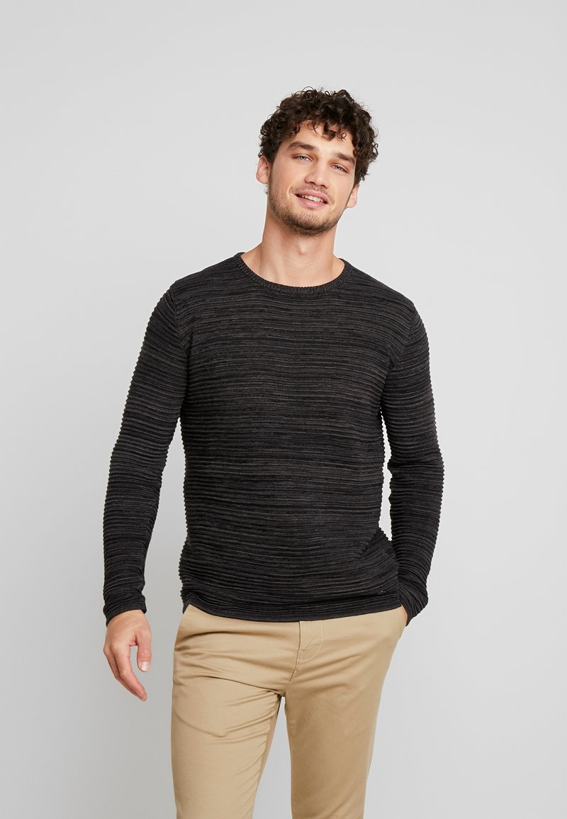 Dark gray knitted sweater with vertical rib texture, round neckline, and long sleeves. Paired with light tan pants.