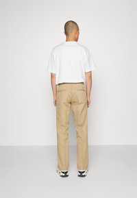Bílý bavlněný tričko a béžové chinos kalhoty se zadními kapsami, doplněné černobílými teniskami. Jednoduchý design, volný střih, žádné viditelné vzory.
