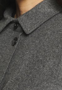Blazer grigio in lana con colletto strutturato, dotato di bottoni neri e una superficie tessurizzata. Il design è sartoriale e aderente.
