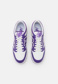 Weiße und lila Sportschuhe mit perforierter Zehenkappe, Schnürdesign und sichtbarem Logo an der Seite und auf der Innensohle, mit kontrastierenden Akzenten.