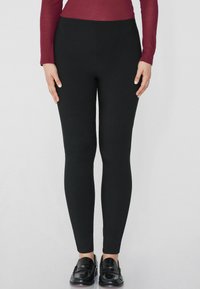 Leggings noirs à coupe slim, fabriqués en tissu extensible. Conception taille haute, texture lisse, sans motifs ni accessoires proéminents.