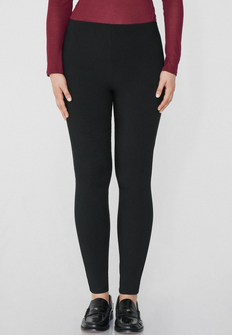 Leggings noirs à coupe slim, fabriqués en tissu extensible. Conception taille haute, texture lisse, sans motifs ni accessoires proéminents.