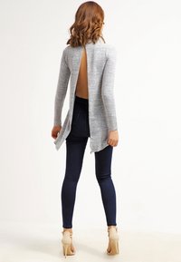 Cardigan gris dos nu à manches longues, fentes latérales et texture côtelée, assorti à un jean skinny foncé et des talons beige.