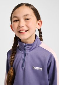 Paars sporttopje met een roze paneel, ritskraag en "hummel PERFORMANCE" logo. Gladde textuur, ontworpen voor actieve kleding.