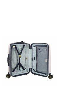 Valigia rigida bianca con accenti blu navy; interno foderato in tessuto a righe, presenta cinghie incrociate, tasche con zip e ruote lisce.