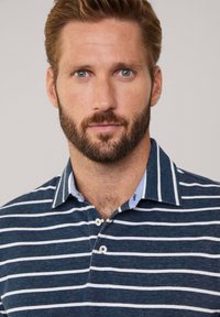 Granatowa polo w paski z białymi liniami, krótki kołnierzyk, dwa guziki i kontrastowy jasnoniebieski wewnętrzny kołnierzyk. Wykonana z fakturowanej tkaniny.