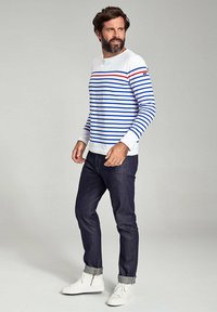 Hvid stribet skjorte med lange ærmer, der har blå og røde linjer, parret med mørk denim jeans og hvide sneakers. Casual pasform, rund halsudskæring.