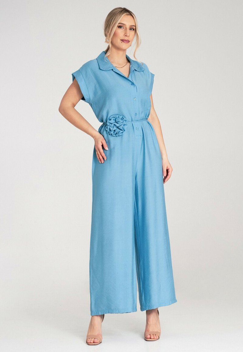 Niebieski lniany kombinezon z krótkimi rękawami, kołnierzykiem, zapinany na guziki z przodu oraz paskiem z detalem w postaci tekstylnego kwiatu. Szeroka nogawka.