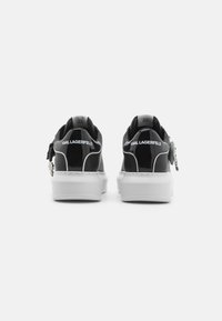 Baskets en cuir verni noir avec des accents et une semelle blanche. Présentent un logo au talon et un détail métallique sur le côté. Forme arrondie.