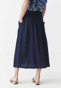 Navy blaue Leinenrock mit fließendem Design, elastischem Bund und seitlichen Taschen. Weiche Textur und knöchellanger Saum. Flache Sandalen abgebildet.