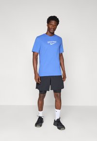 Blå Nike Pro T-shirt med vit logotyp, svarta shorts över kompressionsshorts, vita strumpor och svarta träningsskor. Enkel design.