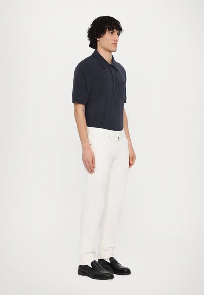 Marinblå velourt-shirt med korta ärmar och en framficka, i kombination med vita jeans och svarta loafers. Enkelt design, strukturerad tyg.
