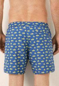 Shorts de bain bleus avec un motif répété de sous-marins jaunes arborant des drapeaux. Taille élastique avec cordon de serrage et poches latérales.