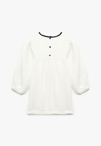 Blusa blanca de manga larga con ribete negro en el escote redondo, tres botones negros en la parte superior de la espalda y mangas abullonadas.