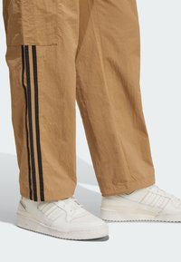 Pantalon cargo beige avec des bandes latérales noires et des baskets blanches dotées d'une tige texturée, d'une languette rembourrée et d'une semelle plus épaisse.