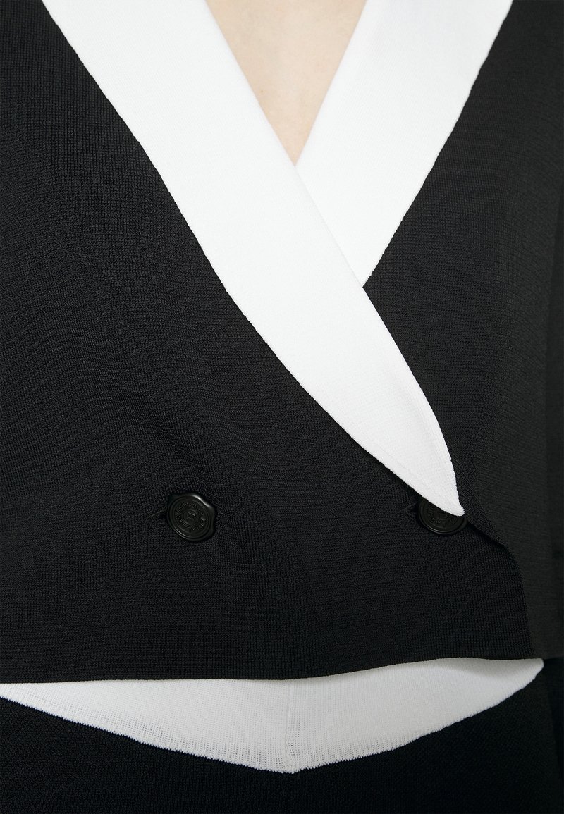 Schwarz-weißer, doppelt geknöpfter Blazer mit breiten weißen Revers und sichtbaren schwarzen Knöpfen, getragen über einem passenden schwarz-weißen Outfit.