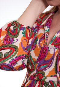Kleurrijke blouse met een paisley patroon in tinten van oranje, roze, groen en paars, knoopdetail op de mouw en gestructureerde stof.