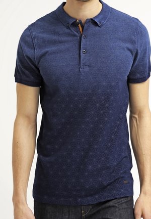 Polo bleu marine à manches courtes, tissu texturé, col boutonné, avec un motif géométrique subtil près de l'ourlet. Détail de fermeture éclair orange.