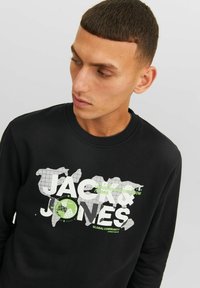 Sudadera negra de algodón, con un diseño gráfico que incluye un mapa del mundo y texto en blanco y verde. Cuello acanalado, mangas largas.