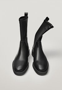 Bottines en cuir noir avec une surface lisse. Elles présentent un bout arrondi et des panneaux latéraux élastiques. Comprennent des tirettes pour un enfilage facile.