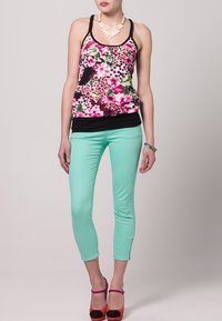 Top senza maniche a fantasia floreale nei colori rosa, nero e verde, sovrapposto a una base nera; abbinato a pantaloni slim verde menta e scarpe col tacco brillanti.
