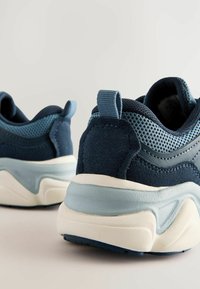Baskets de sport bleu marine avec textures en maille et en daim, dotées d'une semelle bleu clair et d'un onglet au talon pour un enfilage facilité, vues de l'arrière.