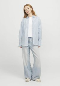 Světle modrá a bílá pruhovaná košile na knoflíky, dlouhé rukávy, volný střih, nošena přes bílý tričko, v kombinaci se světlými širokými džíny.