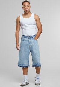 Bermudas de mezclilla azul claro con un corte holgado, dobladillo deshilachado, diseño de cinco bolsillos y cierre de botón. Combinadas con una camiseta sin mangas blanca y zapatillas deportivas.