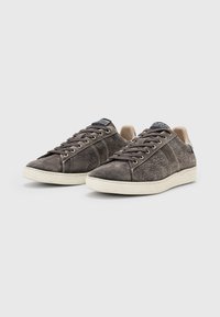 Grå ruskinds sneakers med en struktureret overflade, cremefarvet gummisål og seks metaløjer til snørebånd. Har kontrasterende beige detaljer ved hælen.