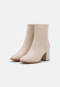 Beige nilkkurit, joissa on pyöreä kärki, sileä pinta, sivusaumat ja paksu lohkoilma. Tehty nahasta ja minimalistisella muotoilulla.