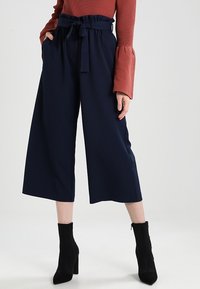 Marinblå vida byxor med en åtsittande midja och knytbälte. Tyget ser slätt ut, med en avslappnad passform och cropped längd.