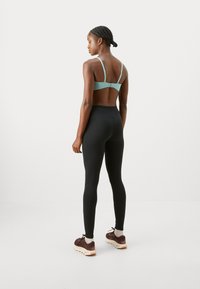Sports bra in light blue with thin straps, paired with black high-waisted leggings and brown athletic shoes. Clean design, smooth texture.