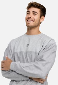 Szary długi rękaw sweter z poziomym jaśniejszym sznurkiem, ściągaczami na mankietach i małą naszywką z logo na klatce piersiowej. Miękka, teksturowana tkanina.