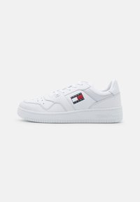 Sneaker bianche con finitura in pelle liscia, dotate di un patch logo rosso, bianco e blu e suola in gomma testurizzata con il marchio "TOMMY".