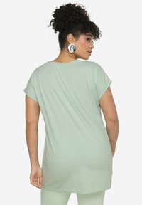 Camiseta de gran tamaño en verde menta con mangas enrolladas, textura suave y dobladillo redondeado, mostrando un ajuste relajado desde la vista trasera.