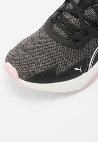 Chaussure de sport tissée noire et grise avec une semelle en caoutchouc rose, dotée d'un dessus texturé, d'œillets de lacets noirs et d'un petit accent de logo.