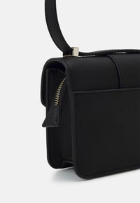 Borsa a mano nera in pelle con una forma strutturata, dettaglio della cerniera dorata e una tracolla corta. Texture liscia con accenti di cucitura. Design compatto e minimalista.