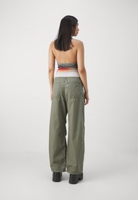 Calças largas verdes com cintura alta e dois bolsos traseiros, combinadas com um top sem alças de várias cores com um padrão ombré.