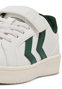 Białe sneakersy z zielonymi akcentami, wyposażone w rzep i sznurowadła, pokazujące zbliżenie na wzór i materiały.