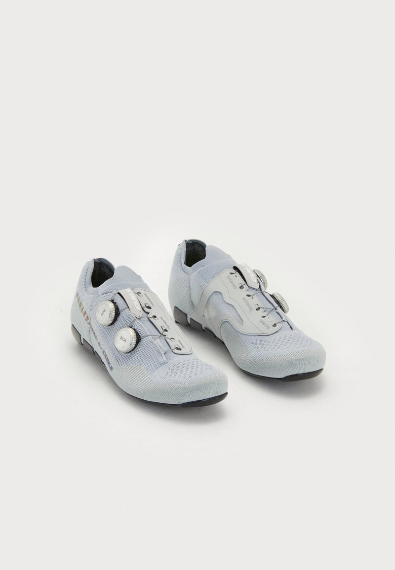 Gaiši pelēki velosipēdu apavi ar elpojošu adītu augšdaļu, diviem regulēšanas dialiem un melnu gumijas zoli ar strukturētu apdari.